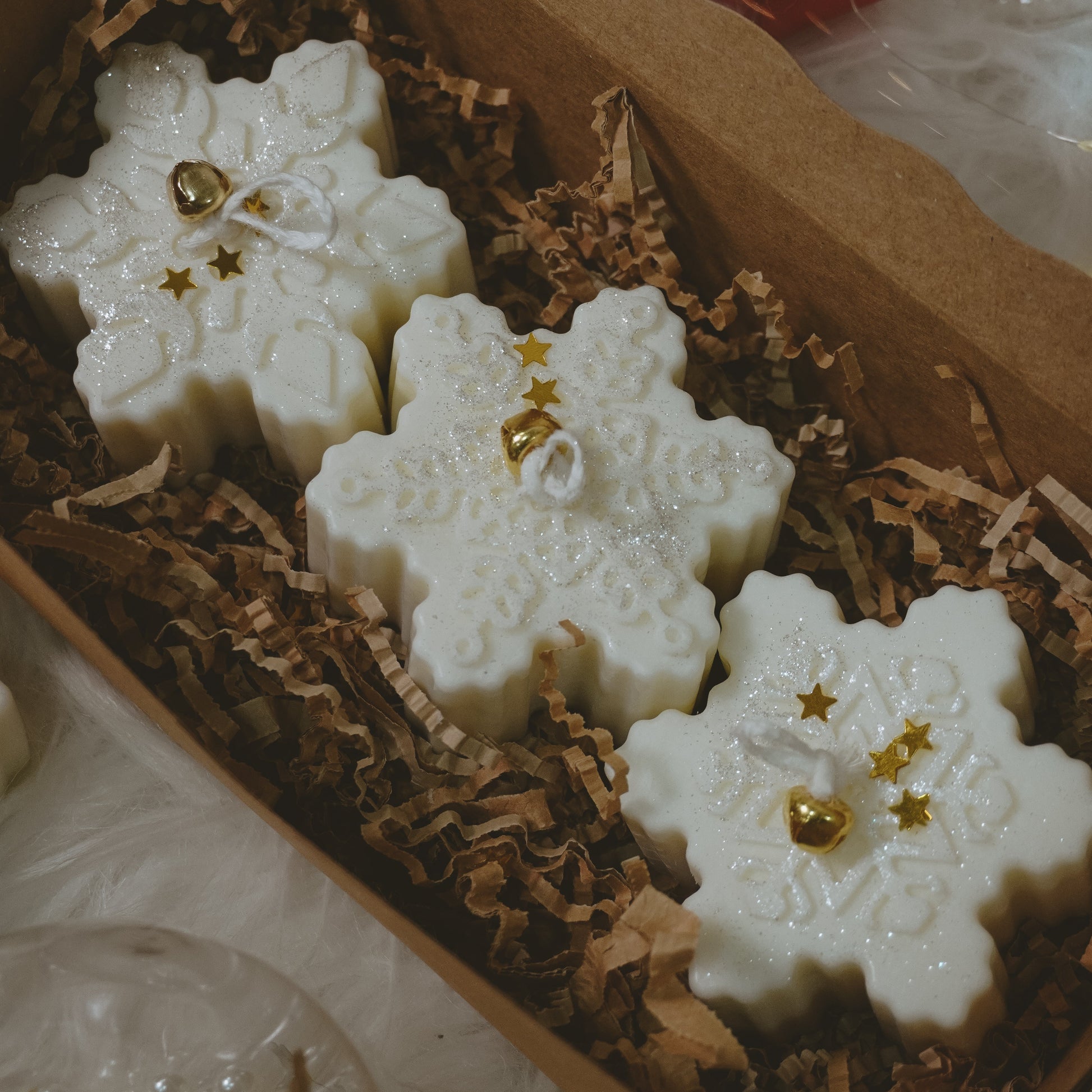 Snowflake-shaped candles with gold accents in a decorative box.