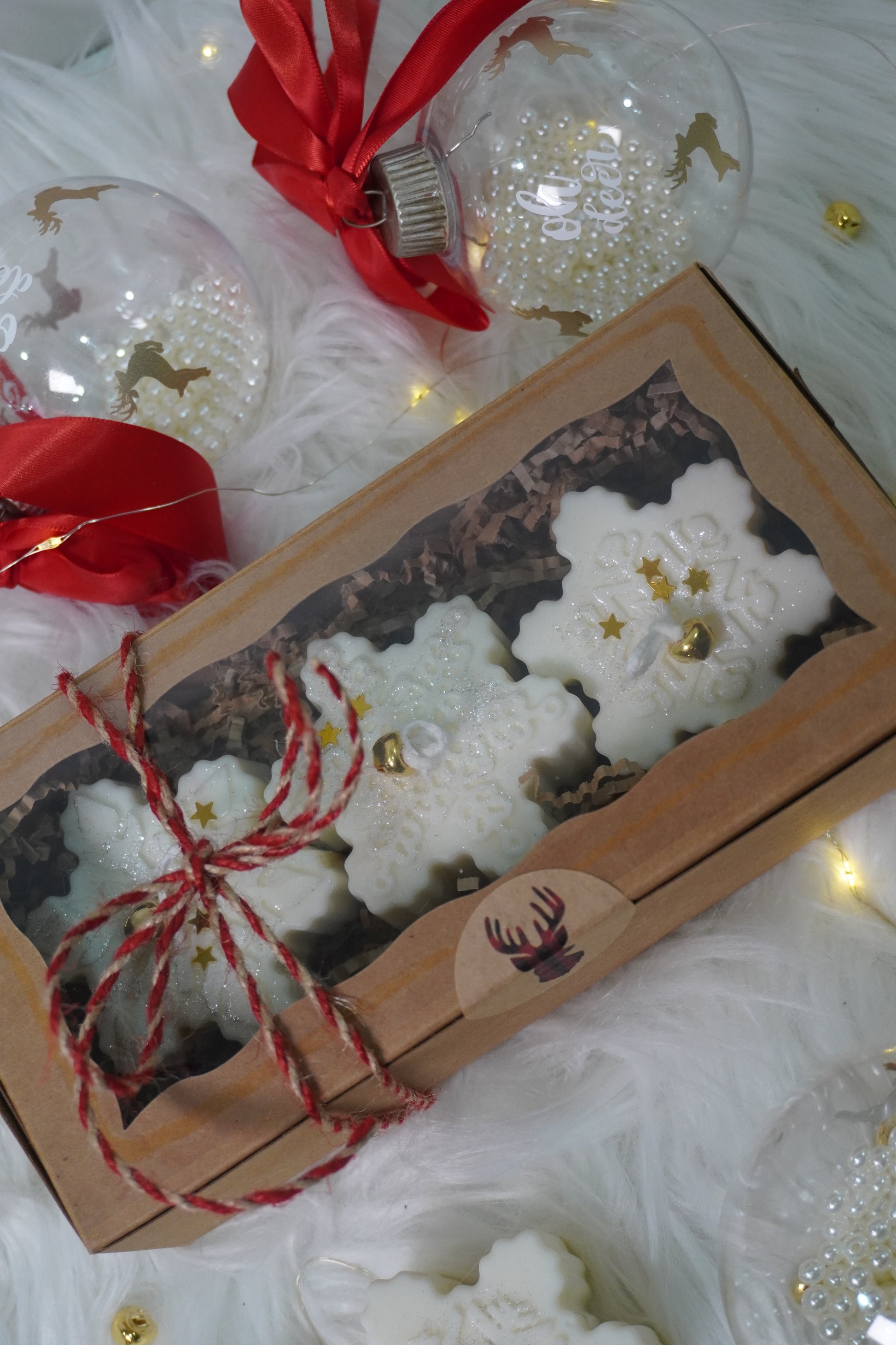 Box of white snowflake-shaped cookies with red string, surrounded by Christmas ornaments on a white background.